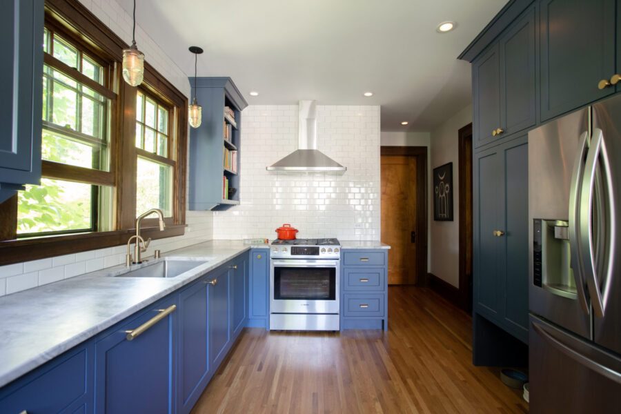 Kitchen remodel uses deep blue cabinetry, white subway tile, wood flooring.