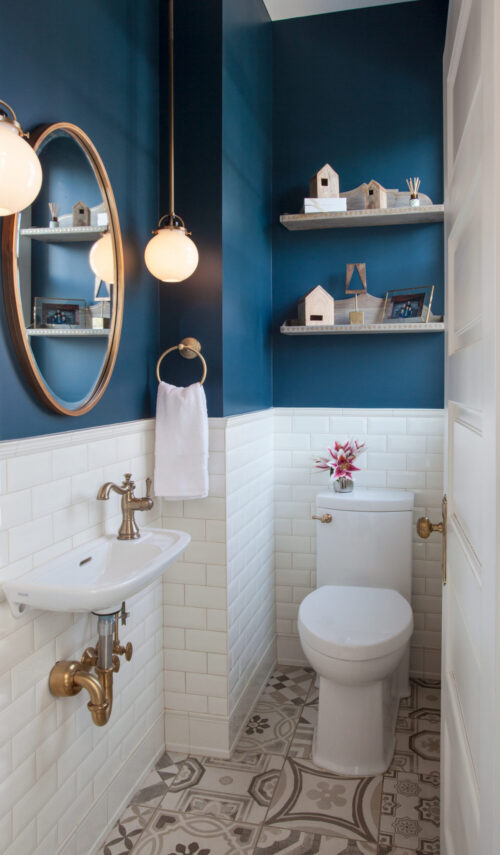 Bathroom features deep-navy-walls, white-subway-tile wainscot, brass fixtures, patterned-cement-tile floor.
