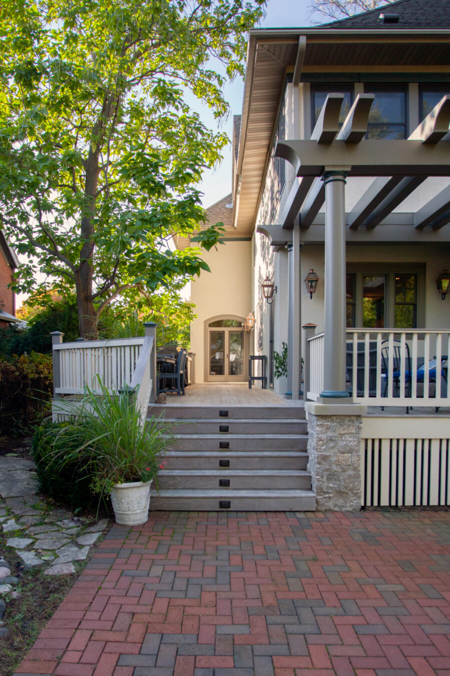 Custom home renovation: multi-level composite deck, step lighting, stone column pergola, brick paver patio.