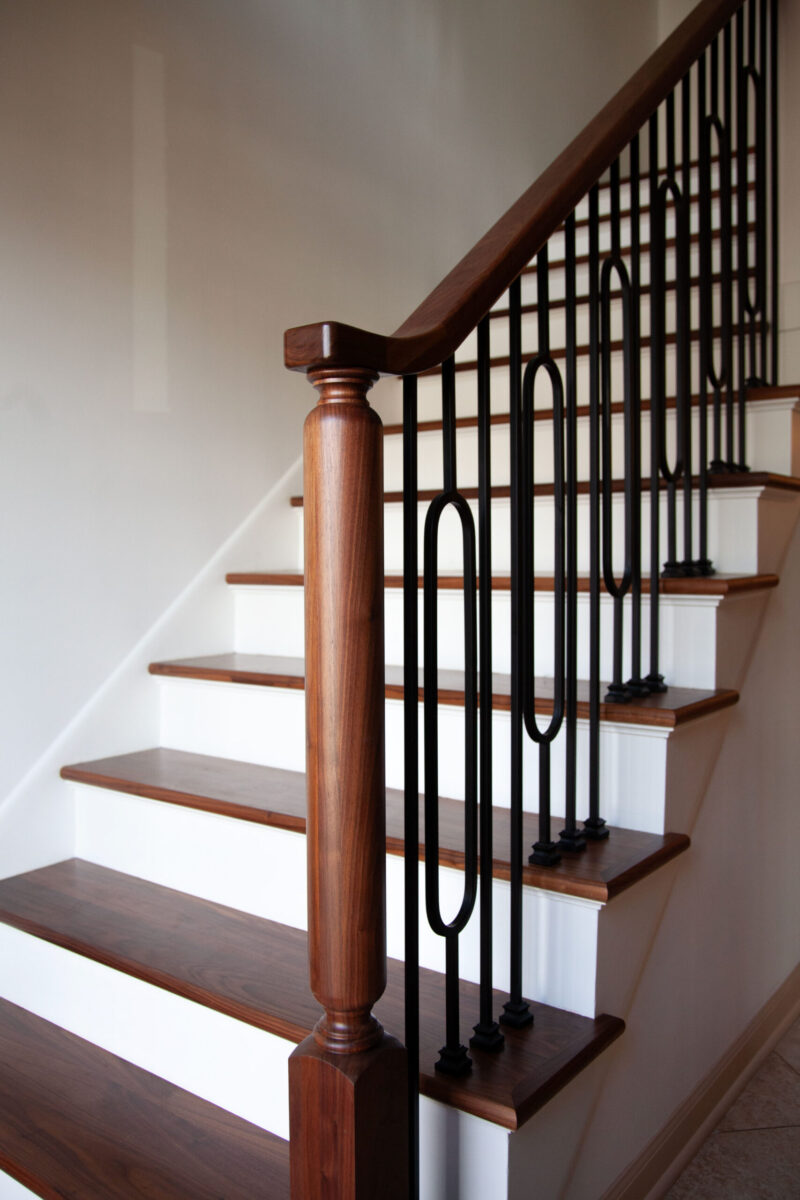 Staircase remodel features dark wood, white risers, and intricate black oval metal balusters.