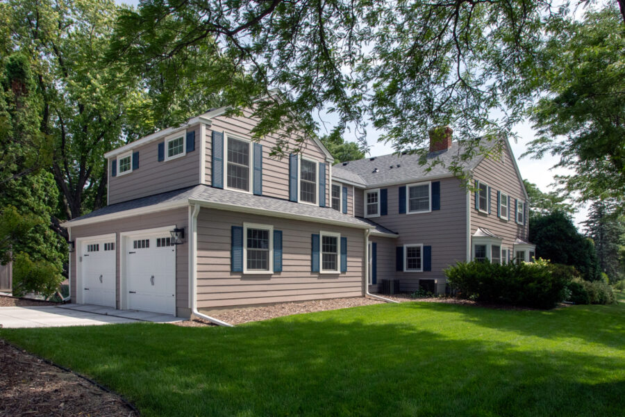 Comprehensively remodeled tan two-story residence features blue shutters, white garage doors.