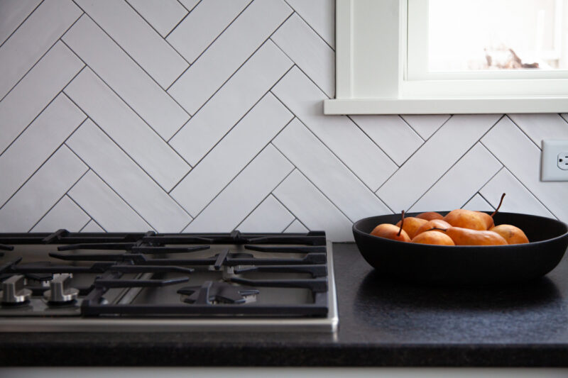 Modern kitchen remodel features herringbone tile, black granite countertop.