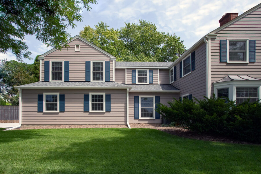 Two-story residential exterior renovation features light-colored siding, dark-blue shutters.
