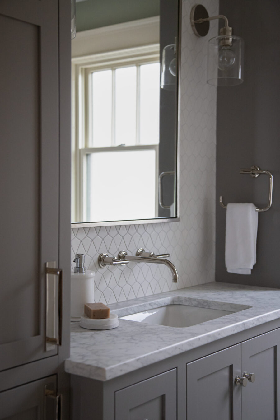 Modern bathroom remodel features gray vanity, white marble counter, geometric tile backsplash. Natural light enters.