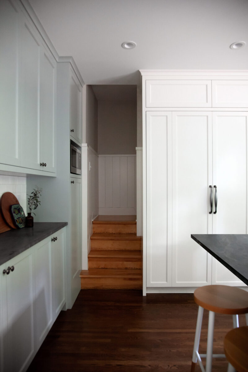 Twin Cities kitchen remodel features white cabinetry, dark counters, wood floors, bright stairs.