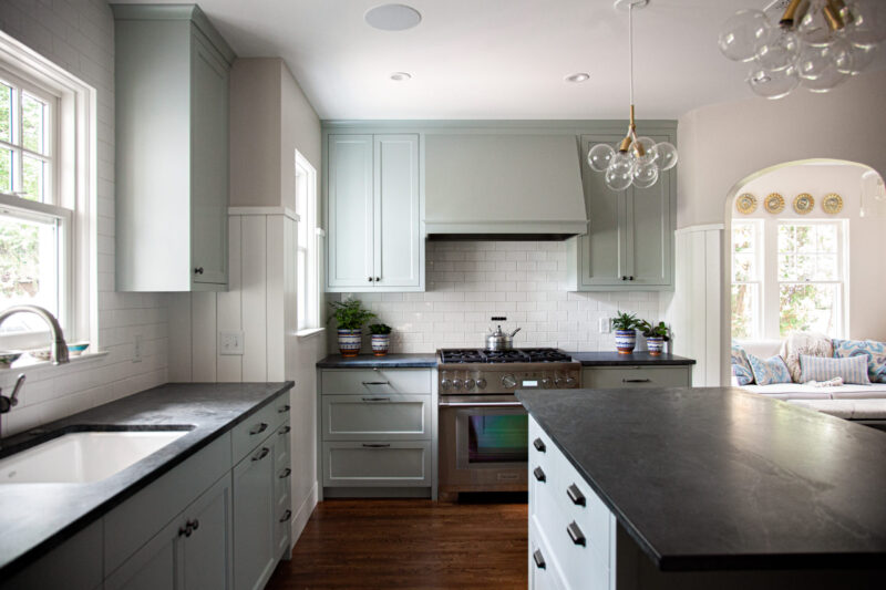 A bright Twin Cities kitchen remodel employs light green cabinetry, dark counters, white subway tile, and a modern range.