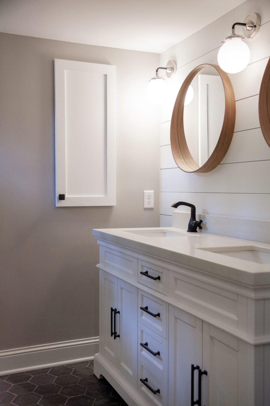 Bathroom remodel: white double vanity, black hardware, quartz top. Round wood mirrors, globe lights, hexagonal floor.