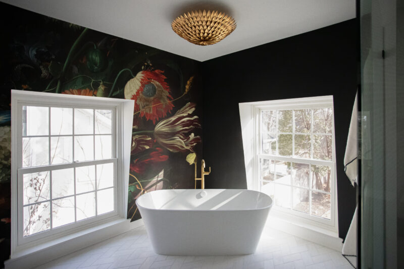 Modern bathroom remodel features dark floral wallpaper, white tub, brass accents.