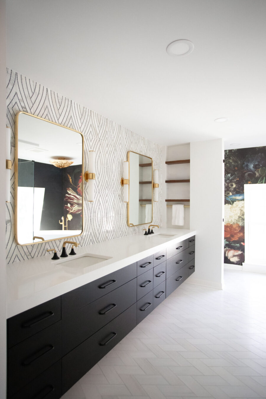 Spacious modern bathroom renovation features dark vanities, gold faucets, striking patterned wall.