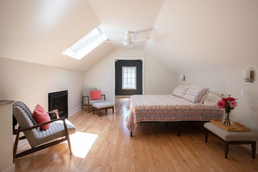 Bright Twin Cities attic bedroom renovation, featuring a skylight, wood floor, sloped ceiling, bed, seating, and built-in fireplace.