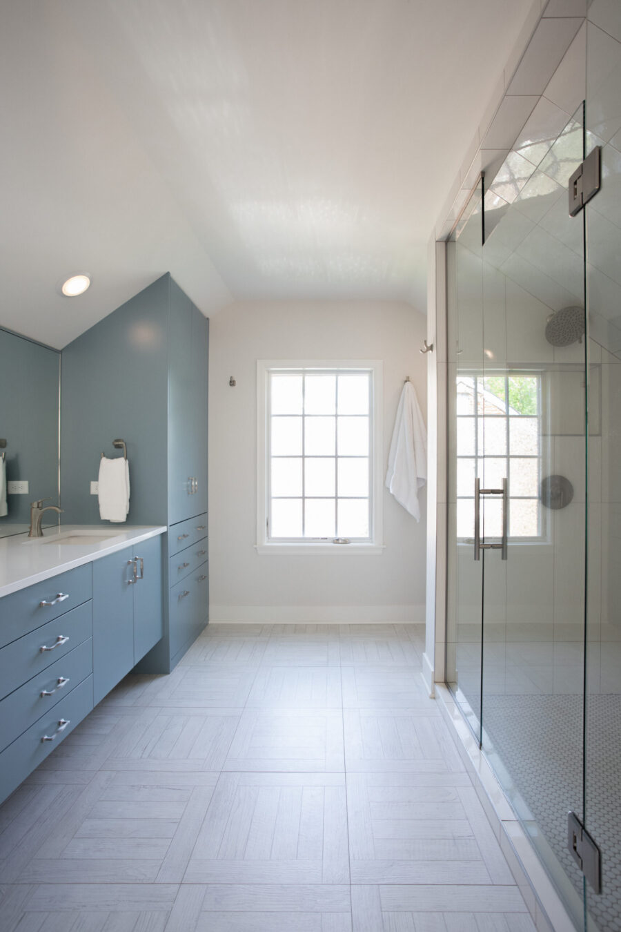 This spacious Twin Cities bathroom remodel features a blue vanity, white countertop, and light gray floor tiles.