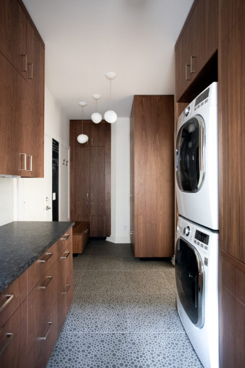 Features stacked-washer-dryer, walnut cabinetry, dark-stone-countertop, globe pendants, pebble-tile floor