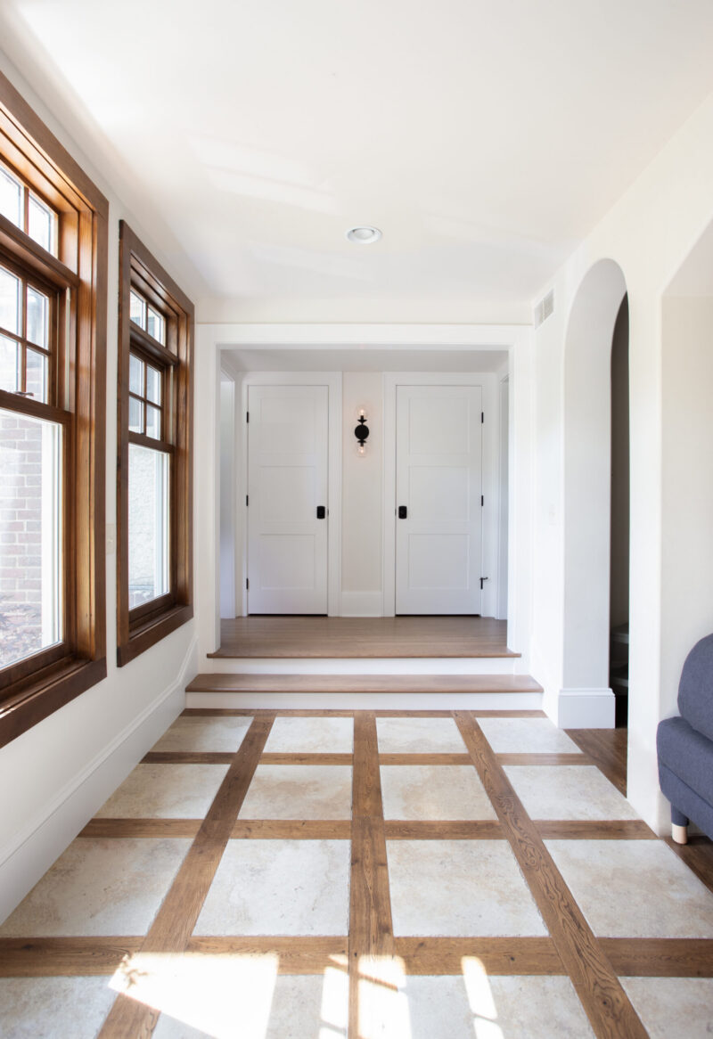 Sunlight illuminates entry-hall: hardwood-framed windows, gridded stone-and-wood floor.