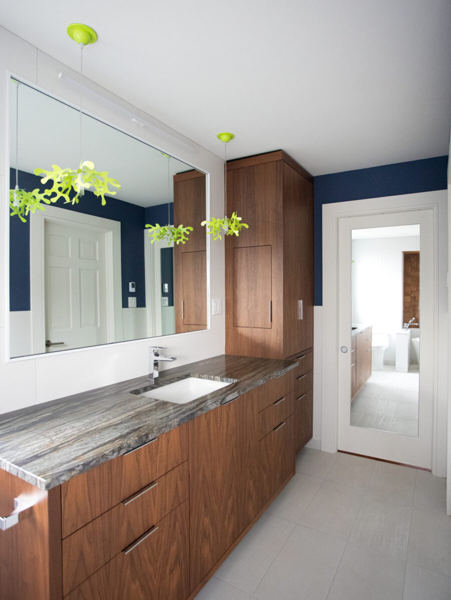 Modern bathroom remodel features dark wood vanity, striated stone, large mirror, green pendant lights. Twin Cities.
