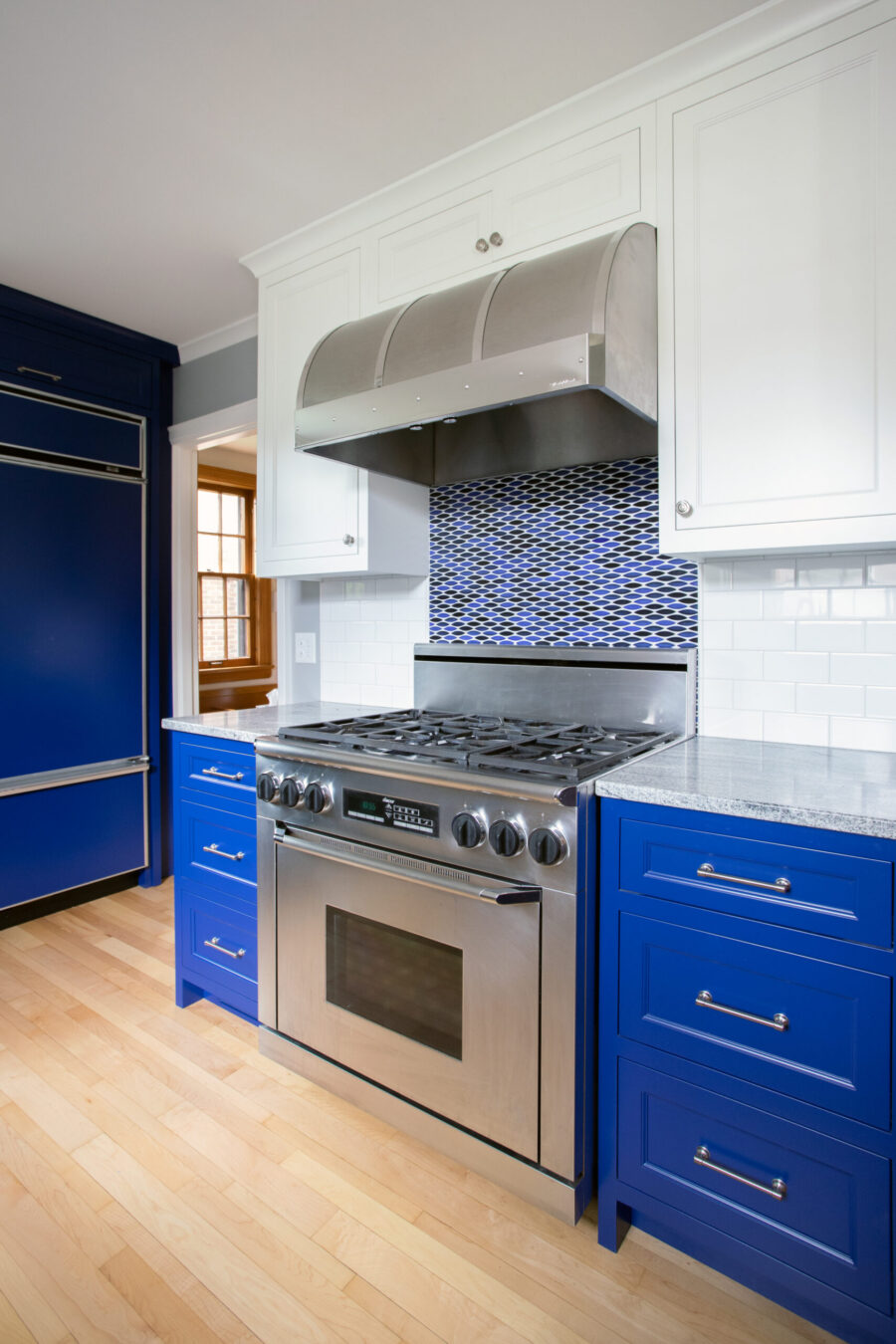 Twin Cities kitchen remodel: blue base and white upper cabinets, stainless range, tile backsplash, and wood floor.