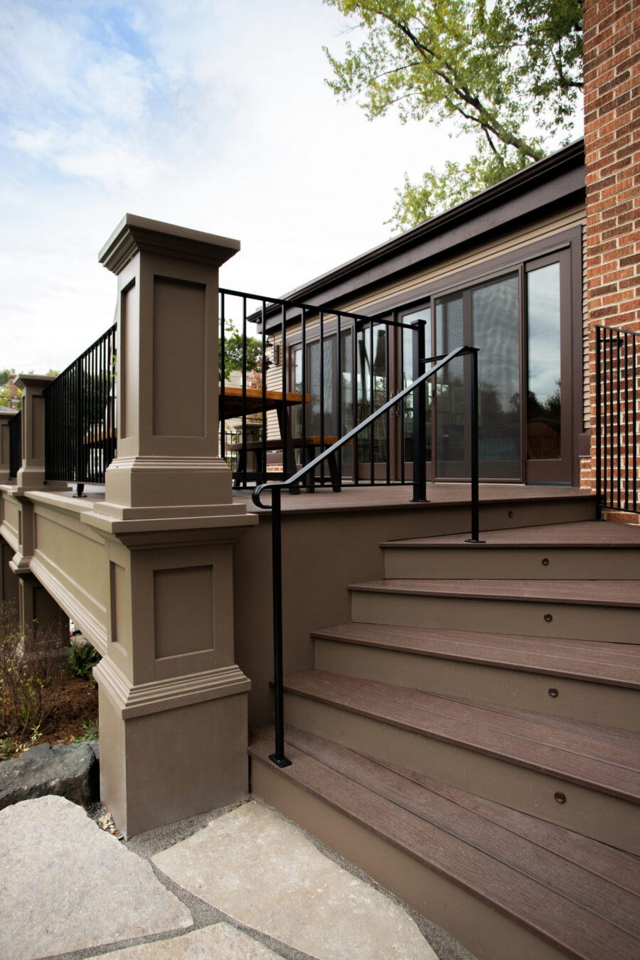 Modern exterior remodel features a multi-level brown composite deck, black railings, taupe pillars, and integrated stair lights.