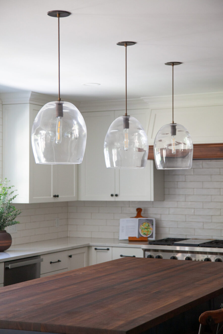Kitchen remodel: glass pendants illuminate dark butcher block, white cabinets.