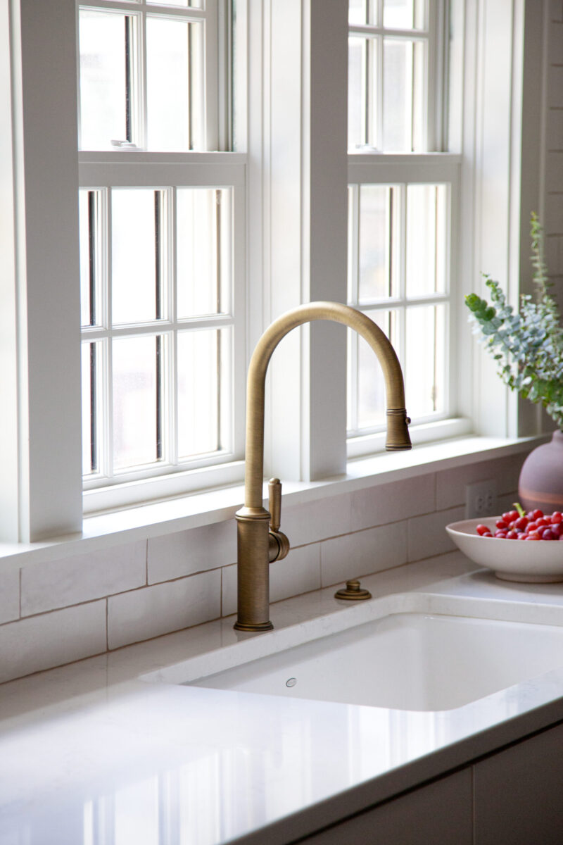 Sophisticated bronze faucet, white tile backsplash, quartz countertop, sunlit kitchen remodel.
