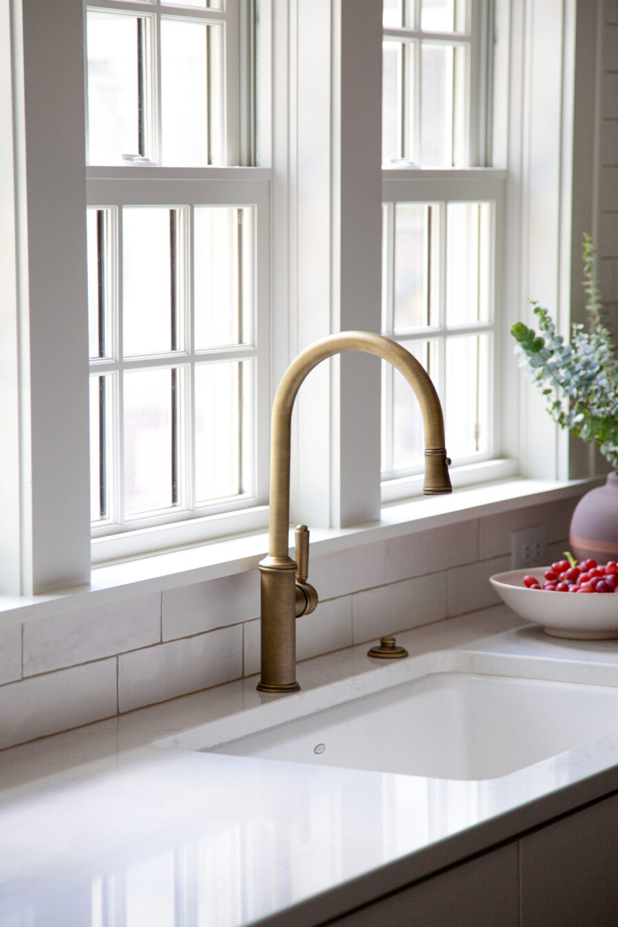 Sophisticated bronze faucet, white tile backsplash, quartz countertop, sunlit kitchen remodel.
