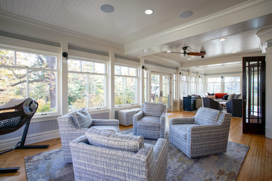 Sunroom renovation features expansive windows, hardwood, beadboard, patterned chairs.