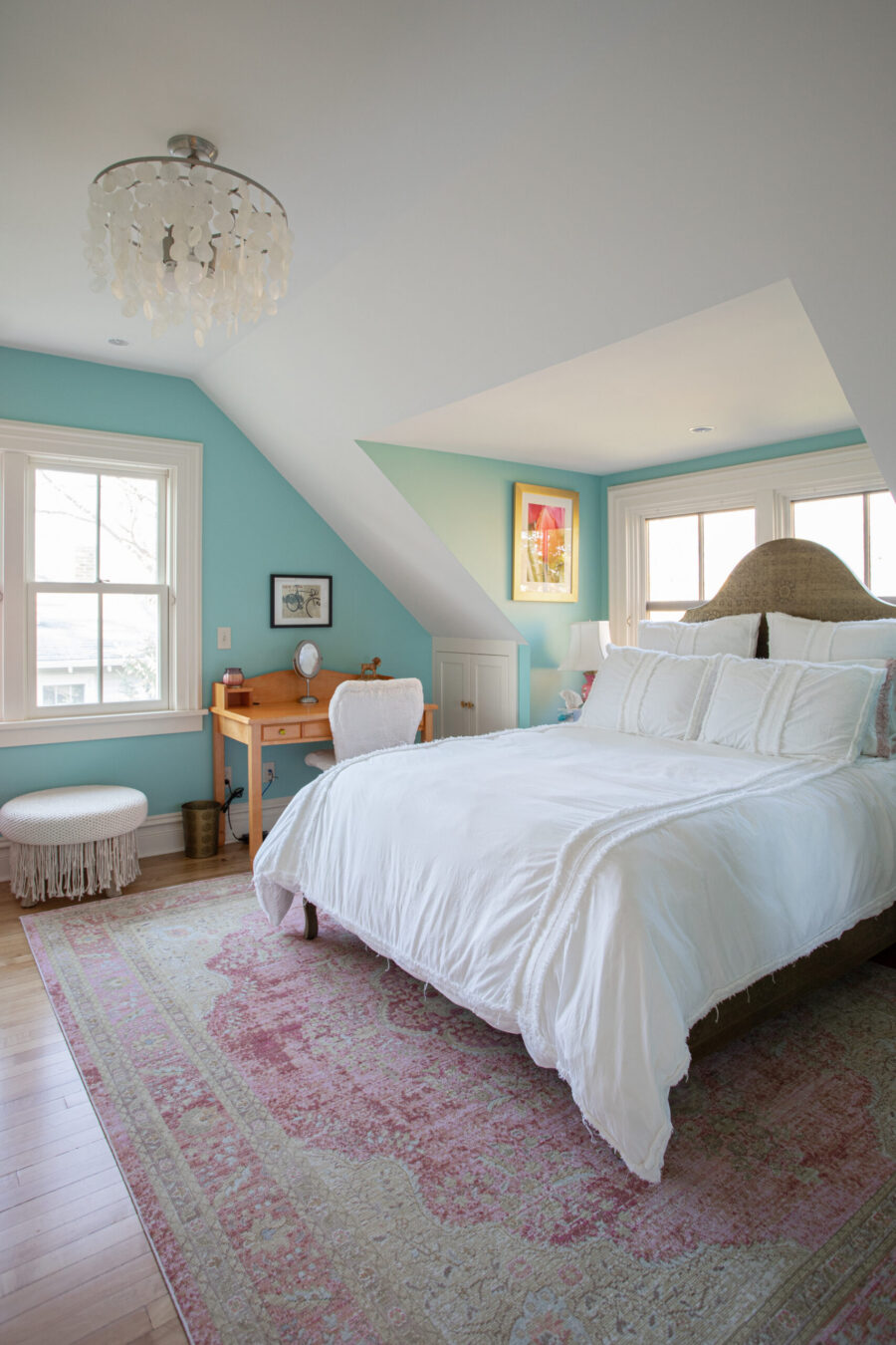 Attic bedroom renovation features sloped ceilings, bright teal walls, light wood flooring, and large windows.