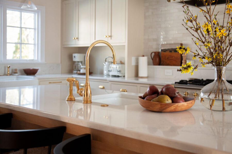 Modern kitchen remodel features white quartz countertops, brass faucet, cream cabinets, tile backsplash.