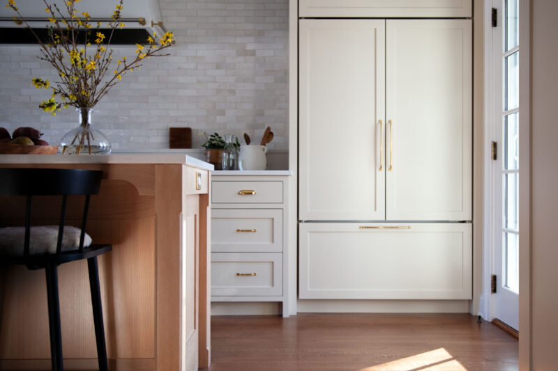Bright kitchen features blonde island, white integrated refrigeration, and subway tile.