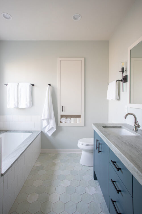 Modern bathroom remodel: blue vanity, sleek tub, hexagonal floor, soft lighting.