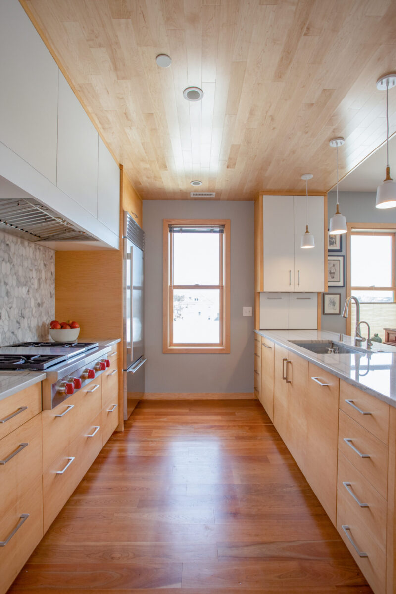 Expansive kitchen remodel presents light timber ceiling, rich hardwood floor, white cabinetry.