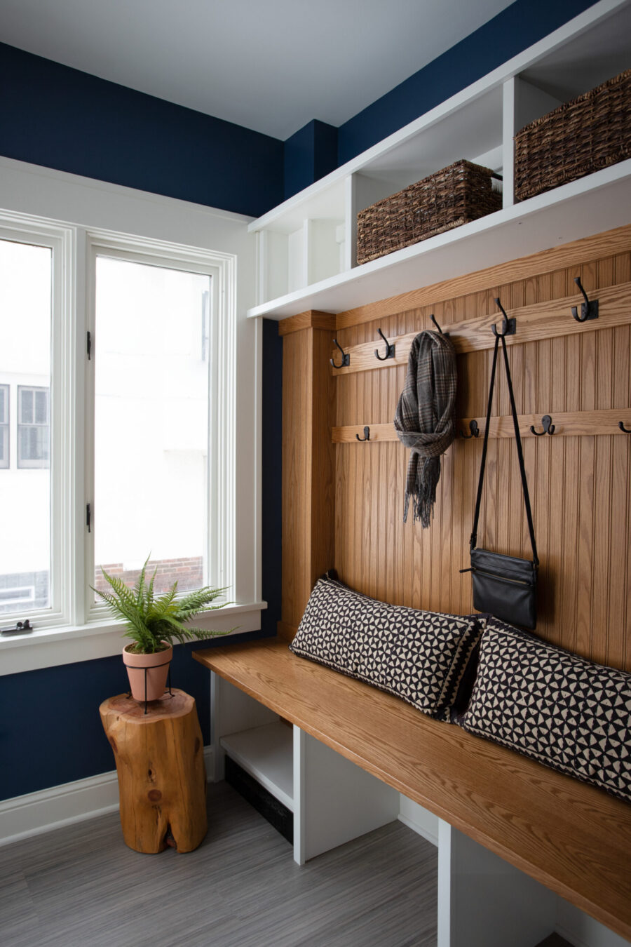 Twin Cities mudroom renovation: bright oak built-in, navy walls, white overhead shelving.