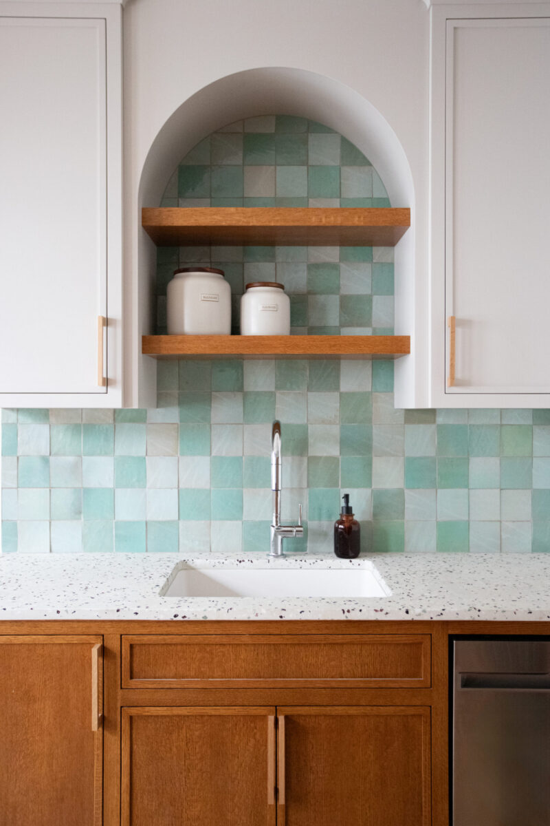 Kitchen remodel: mixed cabinetry, speckled counter, teal-tiled backsplash arch.