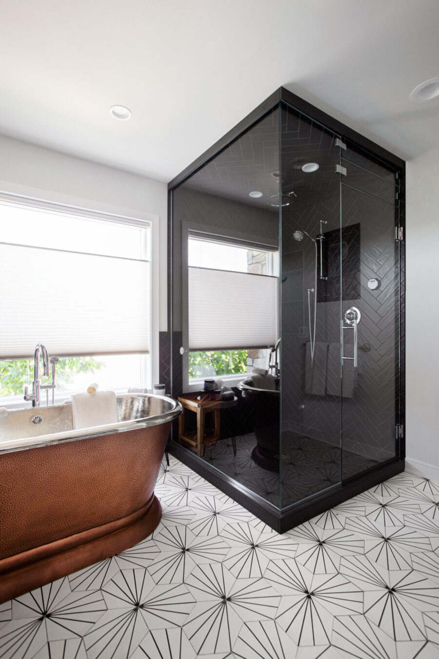 Twin Cities bathroom remodel features a hammered copper tub, dark herringbone tiled shower, and geometric floor tiles.