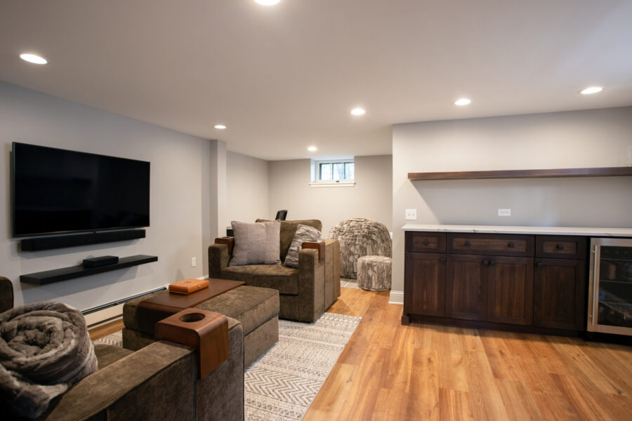 Stylish basement remodel features integrated media, custom built-ins, light wood floors, recessed lights.