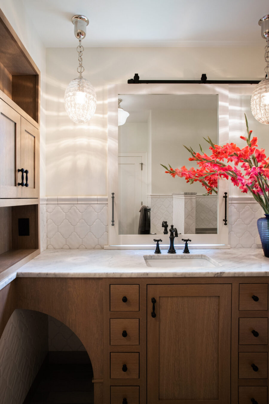A Twin Cities bathroom remodel includes custom wood vanity, marble counter, arabesque tile, and decorative pendant lighting.