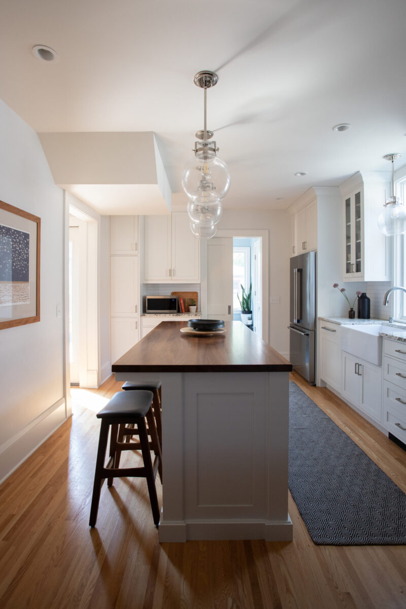 Modern Twin Cities kitchen renovation integrates white cabinetry, dark island, and polished hardwood flooring.