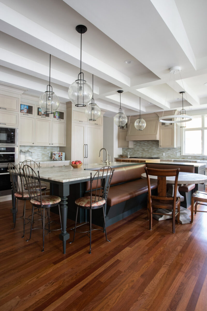 Twin Cities kitchen remodel: coffered ceiling, pendant lights, light cabinets, dark wood floors. Island features banquette seating.