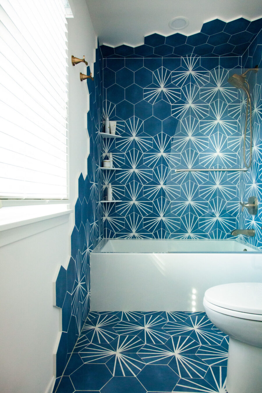 Twin Cities bathroom remodel. Blue hexagonal starburst tiles adorn walls, floor, white tub, and bronze fixtures.