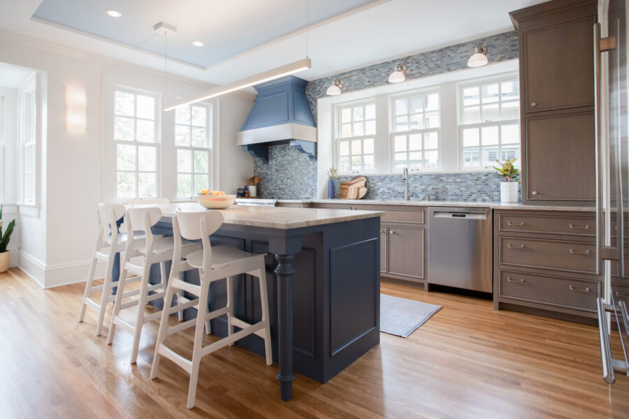Twin Cities kitchen renovation offers navy island, white stools, gray cabinetry, blue mosaic backsplash, timber floor.