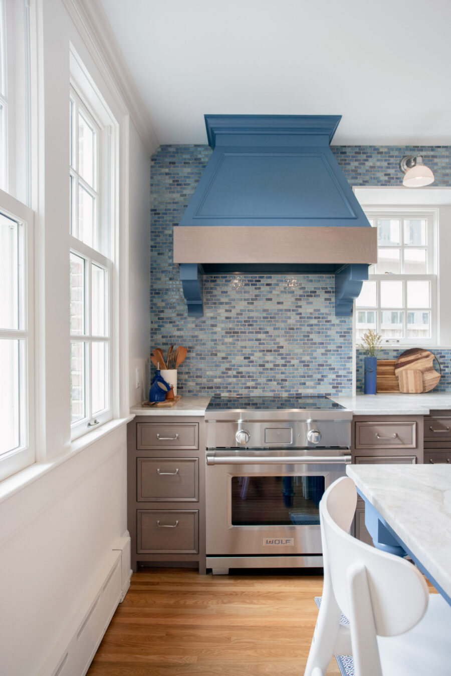 Remodeled kitchen: blue hood, backsplash, stainless oven, gray cabinets, wood floor.