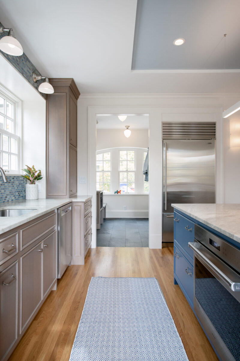 This Twin Cities kitchen remodel combines light taupe cabinetry, a blue island, marble countertops, and polished wood floors, brightly lit.