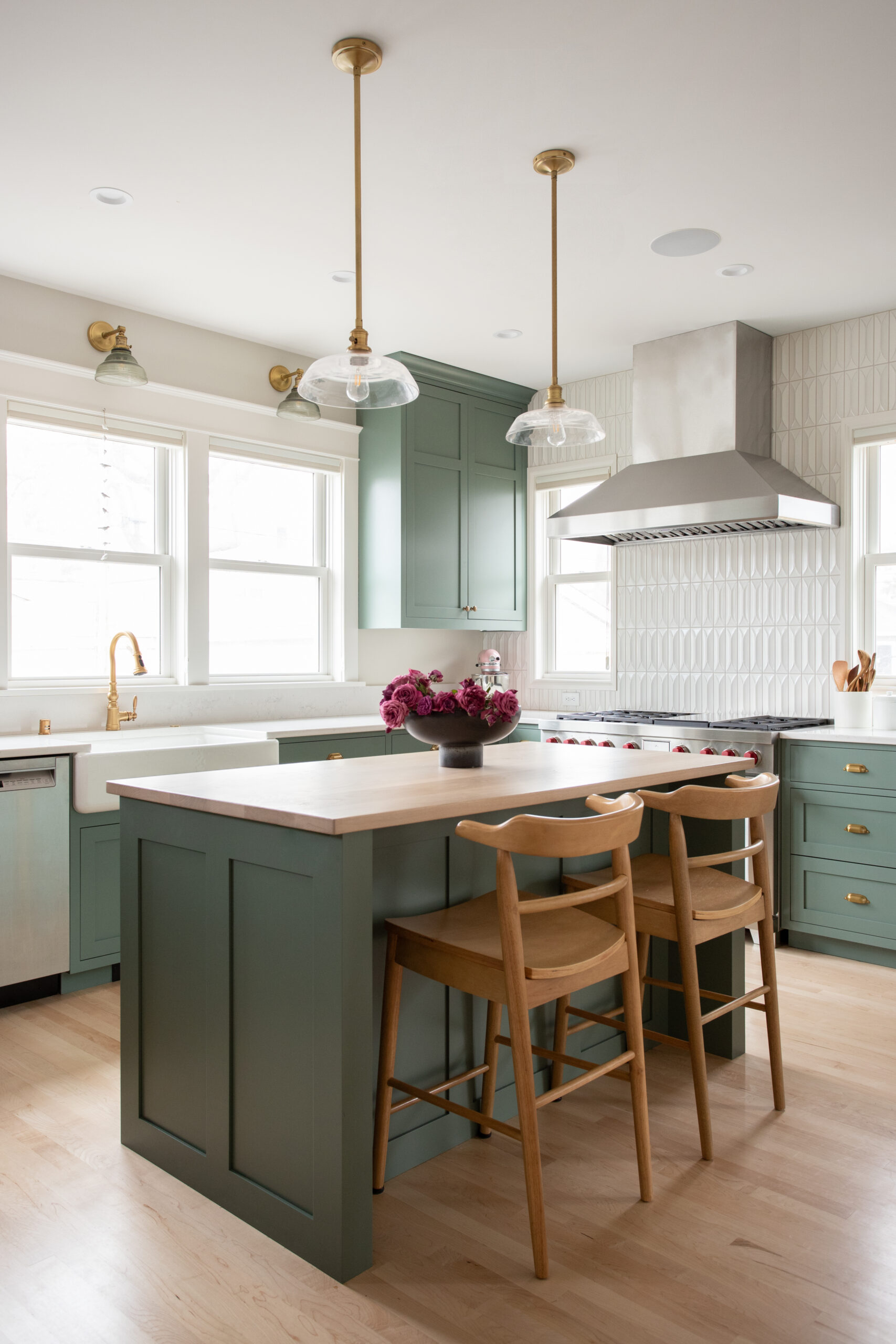 A Twin Cities kitchen remodel features sage green shaker cabinets, brass fixtures, a wood island, and white tile backsplash.