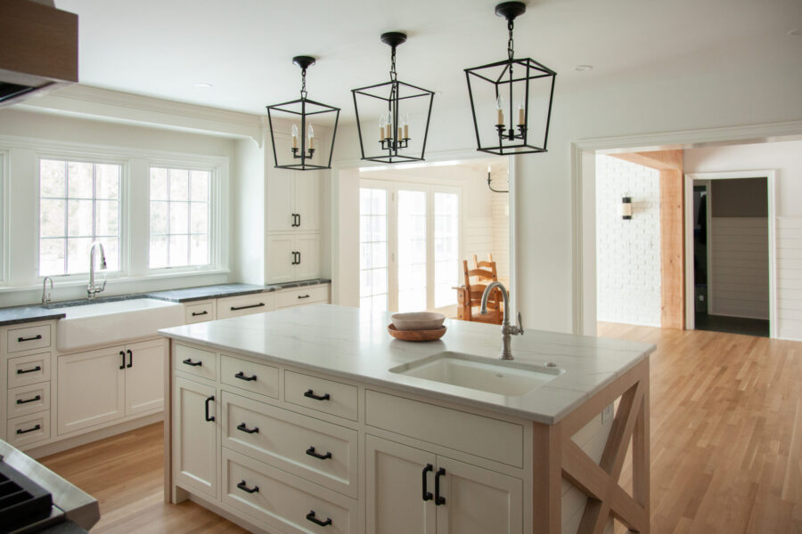 Twin Cities kitchen renovation features white cabinets, island, farmhouse sink, black pendants, wood floors.
