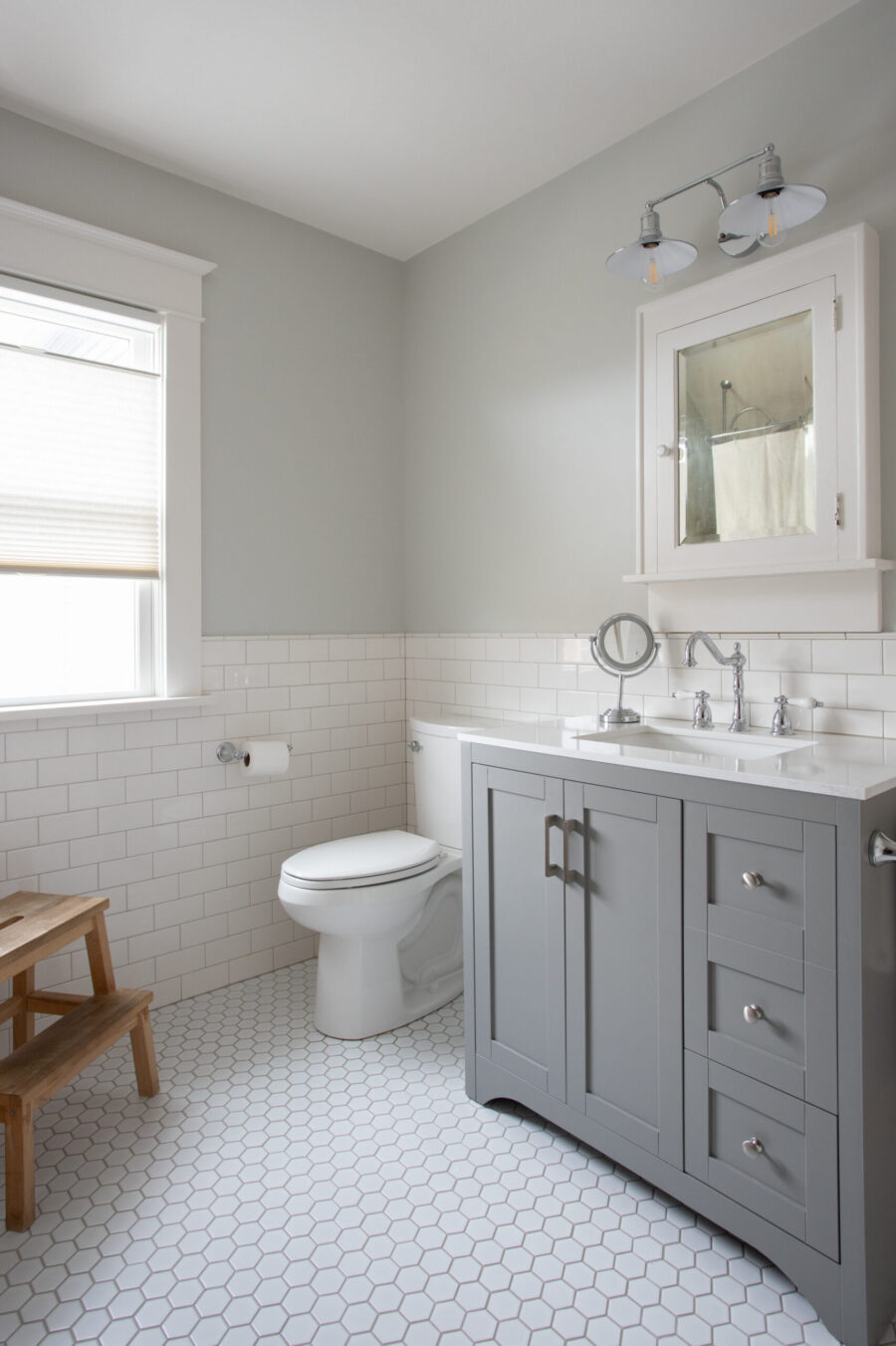 Gray-vanity, subway-tiled bathroom remodel features white hexagonal floor.