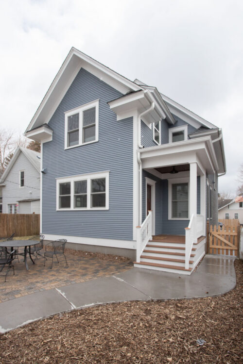 Blue-horizontal-siding house has crisp-white-trim, covered-porch, paver-patio, concrete-walkway