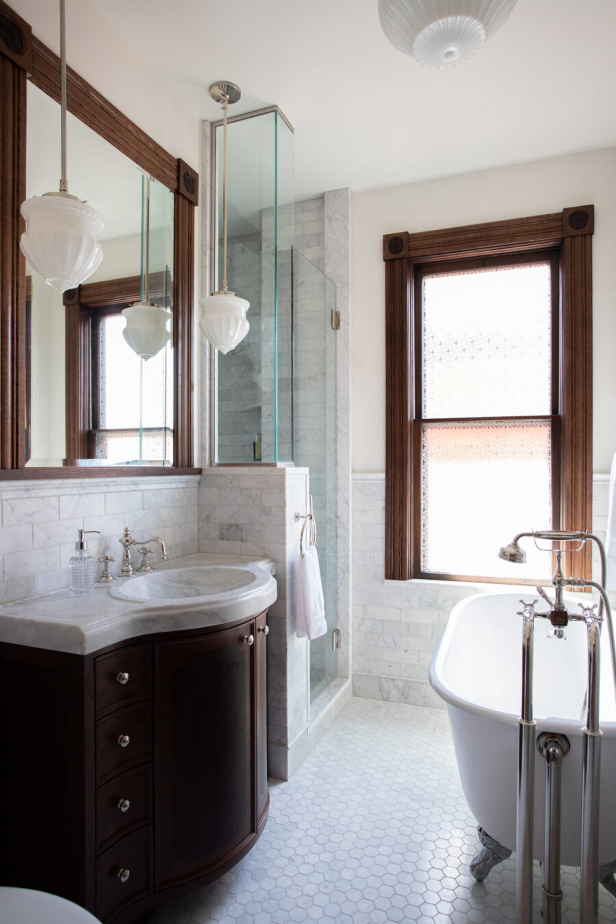 Twin Cities bathroom remodel: dark wood vanity, white marble, glass shower. Freestanding tub on hexagon floor tiles.
