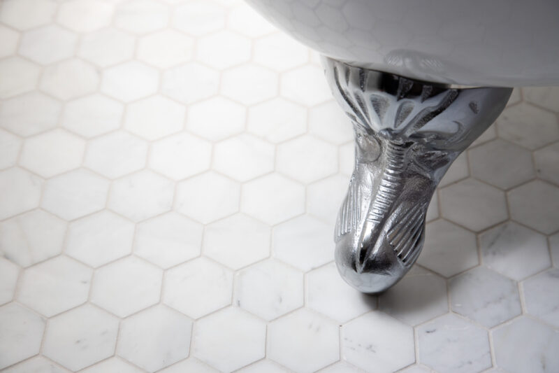 Polished chrome clawfoot supports white hexagonal marble bathroom remodeling.
