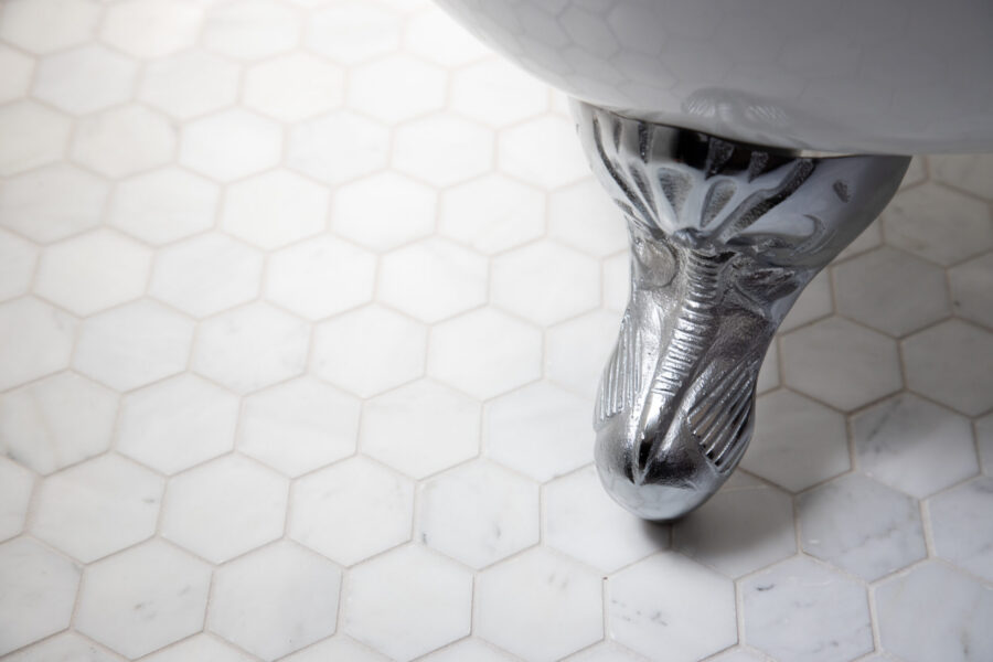 Polished chrome clawfoot supports white hexagonal marble bathroom remodeling.