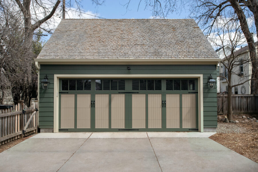 Green detached garage features two-tone paneled doors, dark hardware, and a shingle roof for this home renovation.