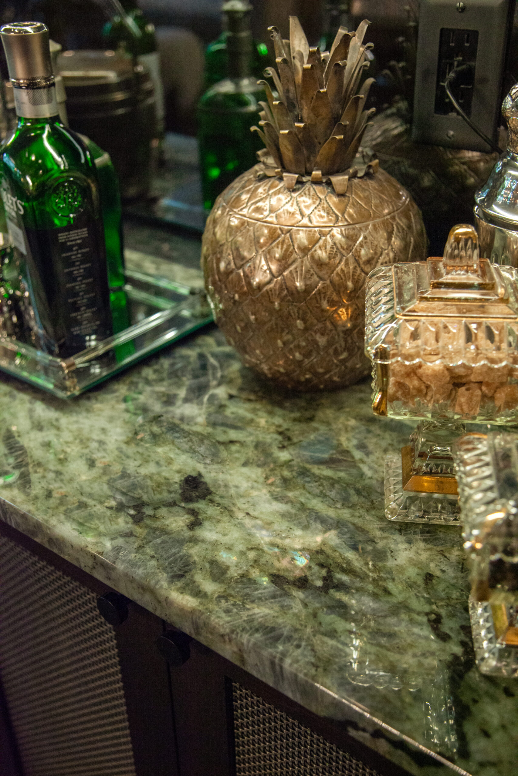 Green-mottled-granite countertop displays metallic-pineapple, glass-bottles. Twin Cities home-renovation design.