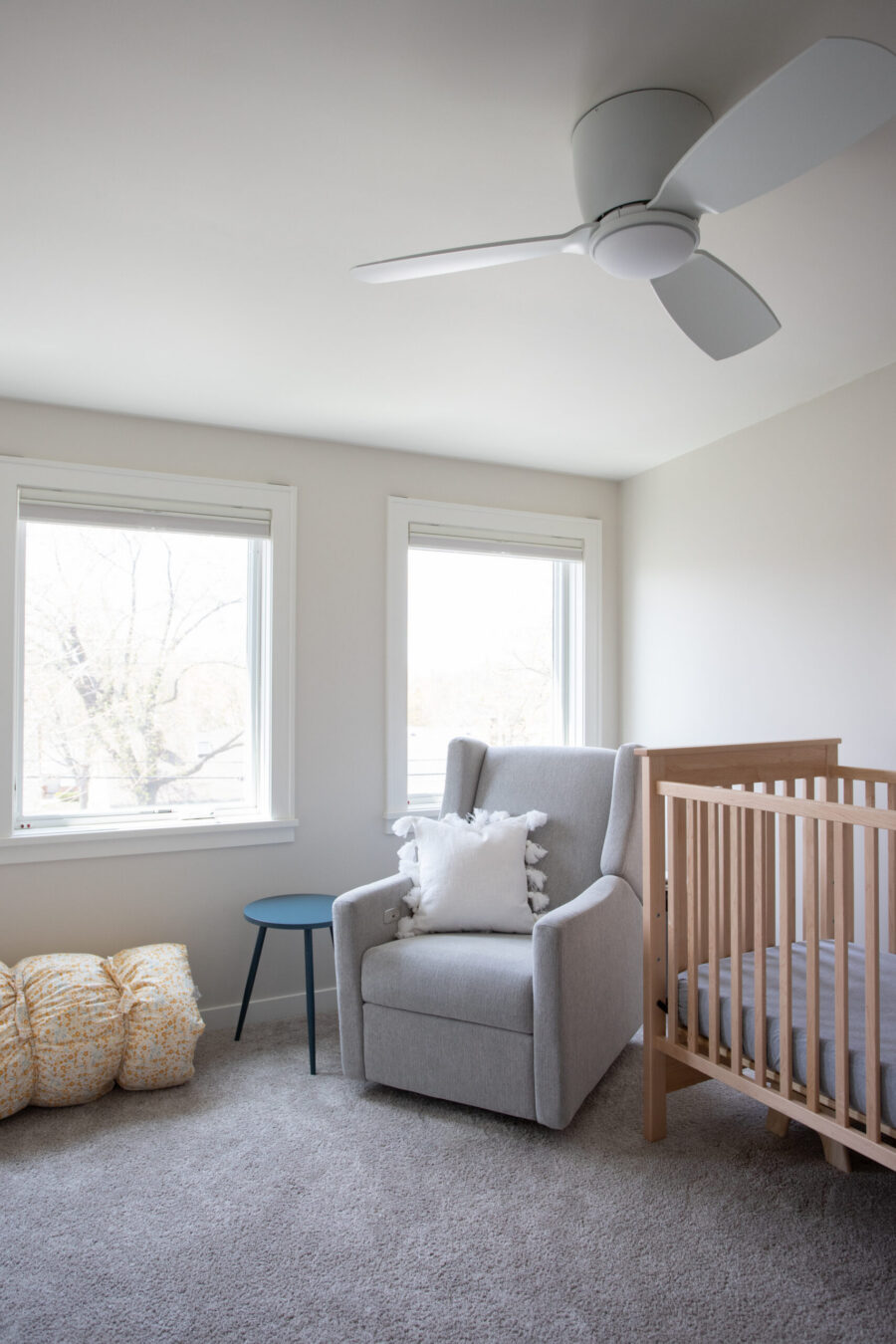 A bright, modern Twin Cities nursery renovation features a gray upholstered glider, natural wood crib, and plush carpet.